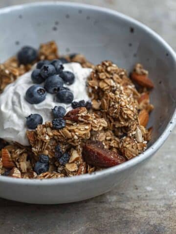 A bowl of toasted sesame granola in a white bowl with yoghurt and blueberries.