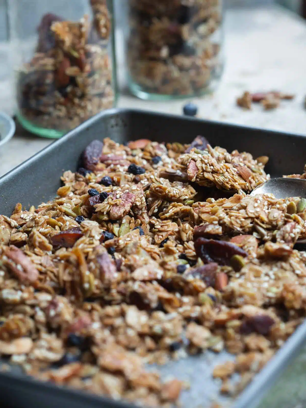 Chunky granola in a baking tray and some packed into nearby jars.